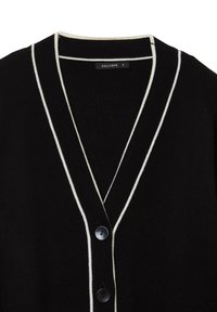 Schwarze Strickjacke mit weißem Besatz entlang des V-Ausschnitts und der Knopfleiste, ausgestattet mit zwei schwarzen Knöpfen und einem kleinen Markenetikett innen.