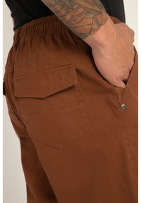 Shorts cargo marron en tissu doux avec une taille élastique, dotés de deux poches arrière et de poches latérales. Design minimaliste.