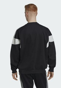 Mustat collegepaidat, joissa on valkoiset raidat hihoissa, ribbaatut hihansuut ja vyötärö. Valmistettu sileästä kankaasta, näyttäen rennon istuvuuden takaosasta.