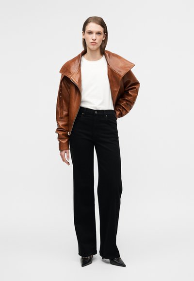 Καφέ δερμάτινο μπουφάν με φαρδιά γιακά, λευκό μπλουζάκι, μαύρο παντελόνι με ίσια γραμμή και μαύρα παπούτσια με μυτερή μύτη. Λείες υφές, ελάχιστες λεπτομέρειες.