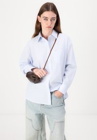 Blå og hvit stripete skjorte med lange ermer, kombinert med lyseblå jeans og en liten brun håndveske.