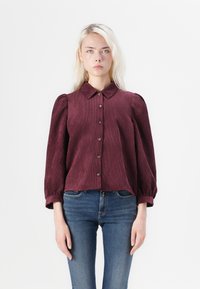 Burgundia värvi korduroüst särk, millel on kraega kaelus, nööbiväli ja puffsleeved. Kombineeritud siniste denimiste teksadega. Sile tekstuur.
