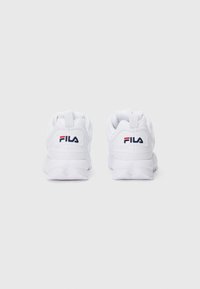 Une paire de baskets blanches FILA vue de dos, avec une semelle épaisse et le logo FILA en rouge et bleu marine sur l'onglet du talon.