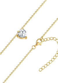 Auksinis grandinės kaklo papuošalas su širdies formos skaidriu akmeniu keturių galiukų laikiklyje. Įeina krabų užsegimas ir reguliuojamas ilgis.