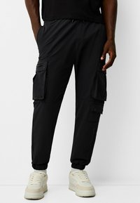 Svarta cargobyxor med elastiska manschetter, flera sidofickor och dragsko i midjan; tillverkade av lätt material.