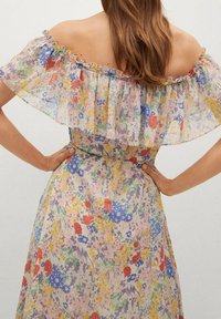 Robe florale décolletée avec des motifs multicolores éclatants, un col volanté et un tissu léger et transparent.