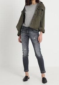 Oliwkowa krótka kurtka, szary t-shirt i przetarte ciemnoszare obcisłe dżinsy. Czarne buty wsuwane. Widoczne naturalne tekstury tkanin.