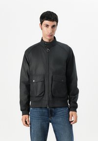 Black bomber jacket with a high collar, front zipper, and two large patch pockets. Features a smooth, slightly textured fabric.