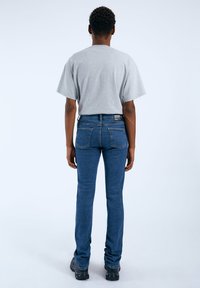 T-shirt grigia a maniche corte abbinata a jeans slim-fit blu scuro. I jeans presentano un design classico con una tasca posteriore visibile e dettagli di cucitura.