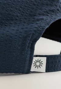 Gorra de tejido azul marina con tela texturizada, visera curvada y etiqueta blanca con un gráfico de sol cerca de la correa ajustable.