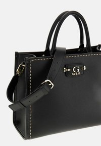 Zwarte faux leren handtas met gouden hardware, bovenhandvatten en een verstelbare schouderband. Heeft contrasterende stiksels en een logo-accent.