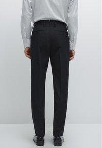 Schwarze, maßgeschneiderte Hosen mit geradem Bein, ausgestattet mit zwei Gesäßtaschen und einer glatten Oberfläche, kombiniert mit schwarzen Schuhen.