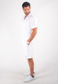 Chemise blanche à manches courtes avec des boutons à l'avant, assortie à un short blanc. Portée avec des baskets blanches, affichant un look décontracté.
