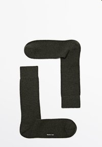 Dunkelgrüne Socken aus einem strukturierten Stoff, mit einem gerippten Bündchen und einem nahtlosen Zehenbereich, versehen mit einem Markenlogo an der Sohle.