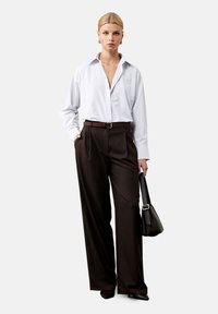Camisa de cuadros en blanco y azul claro, de corte oversize y con un escote en V profundo, combinada con pantalones de cintura alta en marrón, de corte ajustado y un bolso negro.