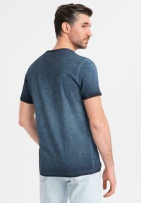 Tmavě modré tričko s gradientem, krátkými rukávy, kulatým výstřihem a jemnou texturou. Disponuje kontrastním černým límcem a okraji rukávů.