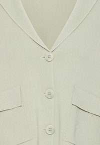 Hele rohelise tooniga kampsun V-kaeluse, viie nupu ja kahe eesmise taskuga. Kangal on sooniktekstuur ja pehme viimistlus.