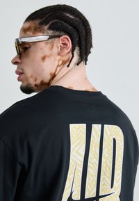 Black t-shirt with large yellow and white patterned "LD" graphic on the back. The wearer is also wearing stylish sunglasses.