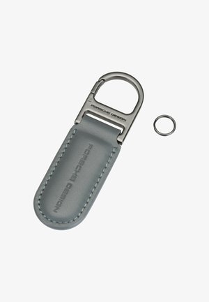 Porte-clés Porsche Design en cuir gris avec fermoir en métal et petit anneau métallique détaché sur fond blanc.