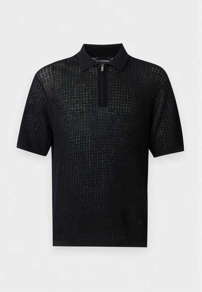 Polo en maille noire à manches courtes avec une texture côtelée, un col et une courte fermeture éclair à l'encolure.