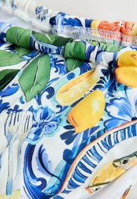 Wzorzyste stroje kąpielowe z żywymi kolorami, w tym żółtymi cytrynami i niebieskimi wzorami kwiatowymi, z marszczoną elastyczną talią.