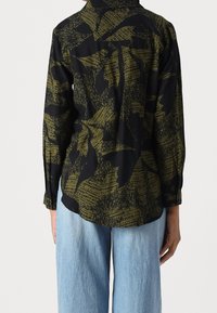Camicia nera con un motivo floreale verde oliva, maniche lunghe, polsini abbottonati e una vestibilità comoda, abbinata a jeans a gamba larga di colore blu chiaro.