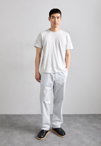 T-shirt en coton gris, coupe ample ; pantalon rayé bleu clair ; sabots noirs avec des semelles en bois. Fond uni. Design simple.