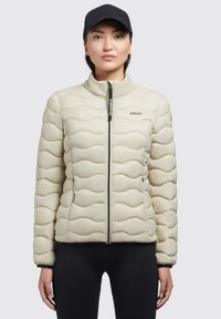 Jachetă puffer matlasată de culoare bej deschis, cu guler înalt, închidere cu fermoar, buzunare laterale și branding KHUJO. Textură netedă și un model subtil de valuri.