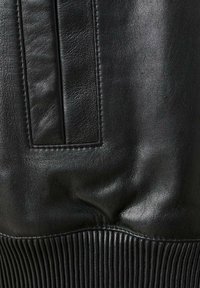 Zwarte leren jas met een gladde textuur, voorzien van een geribde rand en paneeldetails. Focus op de stiksels en strakke ontwerpelementen.