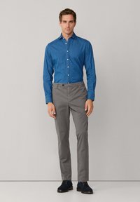 Svetlomodrá džínová košeľa s gombíkovým zapínaním, v kombinácii so šedými formálnymi nohavicami. Oblečenie dopĺňajú tmavé semišové topánky.