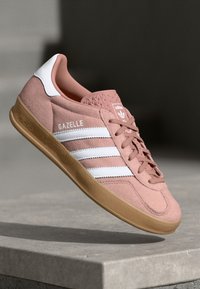 Roza nubuk tenisica s bijelim prugama i detaljima. Ima gumeni potplat i na bočnoj strani ima oznaku "Gazelle". Lagani dizajn.