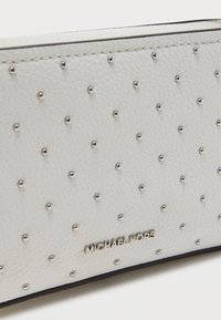 Λευκό δερμάτινο πορτοφόλι με υφή και ασημένιες καρφίτσες, με μεταλλικό λογότυπο. Συμπαγής, κομψός σχεδιασμός με μαύρο περίγραμμα.