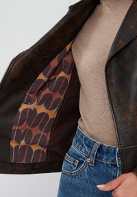 Giacca di pelle marrone con chiusura a zip, caratterizzata da una fodera a motivo audace in tonalità di marrone, giallo e arancione. Esterno testurizzato.