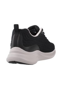 Scarpa sportiva nera a maglia con tomaia testurizzata e suola bianca arrotondata, dotata di un cinturino sul tallone per facilitare l'indosso.