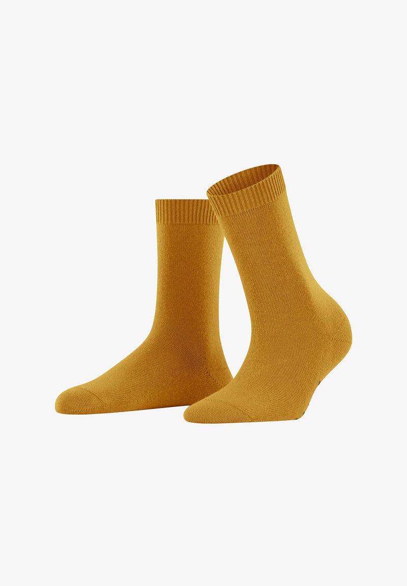 Un paio di calze color giallo senape a metà polpaccio con risvolti a coste, esposte su uno sfondo bianco.