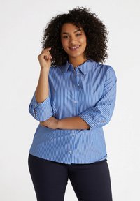 Camisa de botones a rayas azules con cuello extendido, mangas tres cuartos y un corte holgado. Presenta botones blancos y puños doblados.