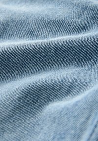 Világoskék farmeranyag lágy textúrával, finom halszálkamintával és sima felülettel, amely finom varráselemeket mutat be.