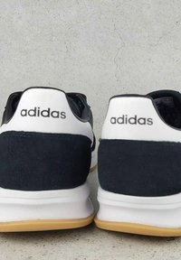 Crno-bijeli Adidas tenisice s nubuk petom, gumenenim potplatom i obloženim ovratnikom s logom na stražnjoj strani.