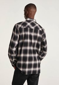 Camicia a maniche lunghe in plaid bianco e nero, con colletto button-down, orlo arrotondato e tessuto testurizzato con una finitura morbida.
