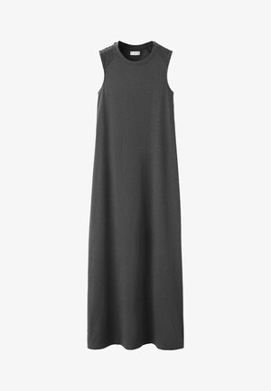 Mladi žena s dugom tamnom kosom, odjevena u crni top bez rukava, zamišljeno gleda u kameru na jednobojnoj bijeloj pozadini.