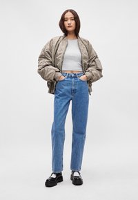 Srebrna bomberka, szary crop top, niebieskie jeansy z wysokim stanem, masywne czarne buty, z białymi skarpetkami, przedstawiające swobodny styl ubioru.