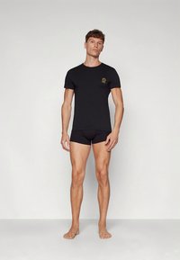 Juoda aptempianti marškinėlių su trumpomis rankovėmis ir apvalia iškirpte, derančia su atitinkamais aptemptais šortais. Marškinėliuose yra mažas auksinis logotipas.