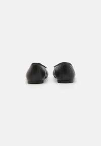 Svarte lær flate sko med avrundede bakstykk, minimalistisk design, og ingen synlig maskinvare. Glatt tekstur med subtile sømdetaljer.