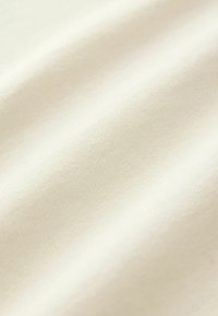 Cremefarvet stof med en glat, let struktureret overflade, der har subtile folder og et ensartet udseende, hvilket antyder blødhed og fleksibilitet.