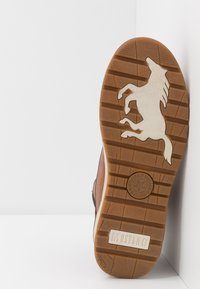 Brązowa podeszwa buta z wypukłym wzorem konia mustanga oraz wytłoczonym logo marki Mustang na gumowej podeszwie.
