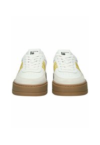 Baltos sportbačiai su geltonomis šoninėmis juostelėmis, storomis rudi pado apačiomis, baltais raišteliais ir „BLCKSTN“ logotipu liežuvėlyje, matomi iš priekio.