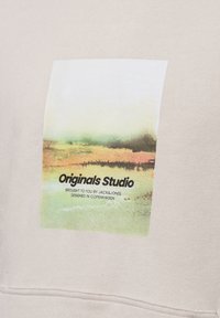 Felpa beige con una stampa grafica rettangolare che rappresenta un paesaggio e il testo: "Originals Studio" in nero, con una texture morbida.