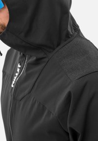 Man wearing black hooded jacket with textured shoulder patch and visible "MILLET" logo along the zipper.