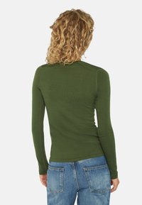 Olivengrøn langærmet skjorte lavet af et blødt, tekstureret stof. Har et fitted design med enkel syning og afrundet nederste kant, parret med blå jeans.