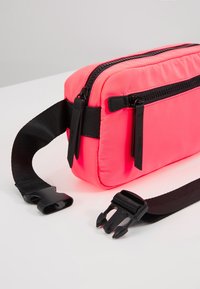 Sac rectangulaire rose néon en matériau synthétique, doté de fermetures éclair noires, d'une sangle ajustable et d'accents métalliques noirs.